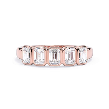 A picture of a five stone diamond wedding ring with emerald cut diamonds that are bezel set in rose gold on a white background with the ring facing forward, lying down.
