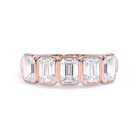 A picture of a five stone diamond wedding ring with emerald cut diamonds that are bezel set in rose gold on a white background with the ring facing forward, lying down.