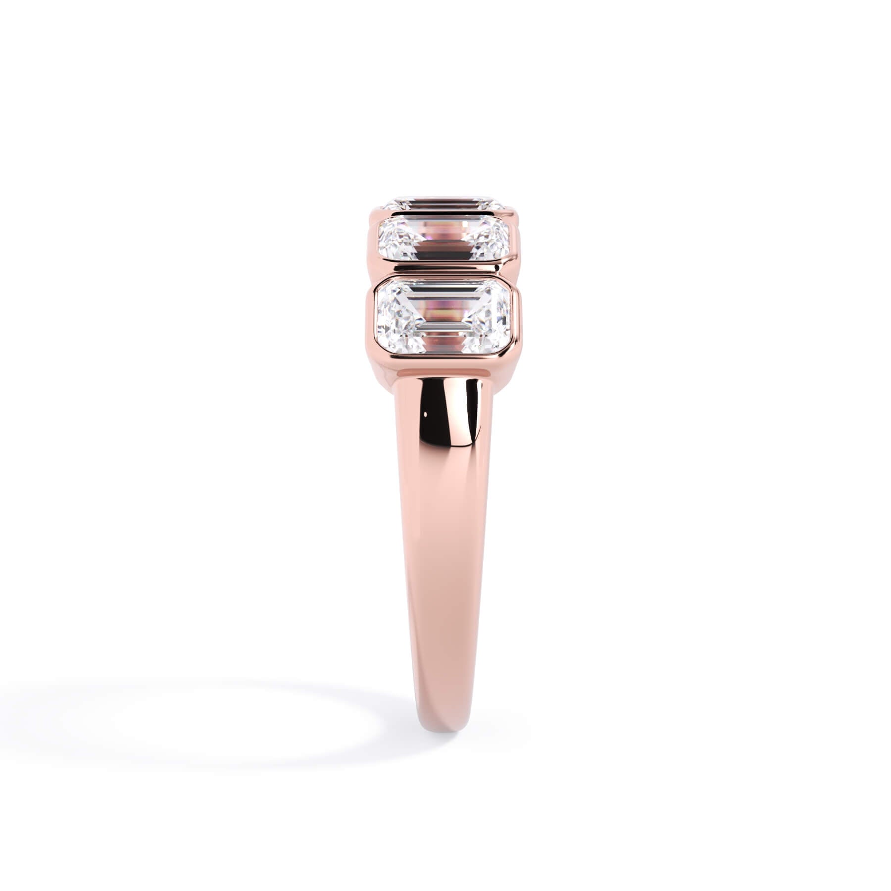 A picture of a five stone diamond wedding ring with emerald cut diamonds that are bezel set in rose gold on a white background with a side profile view.