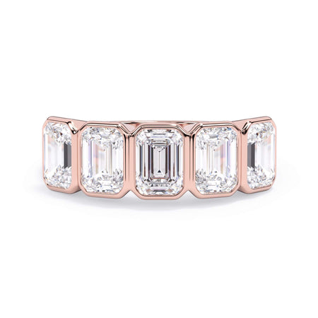 A picture of a five stone diamond wedding ring with emerald cut diamonds that are bezel set in rose gold on a white background with the ring facing forward, lying down.