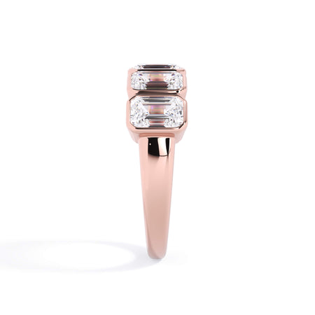 A picture of a five stone diamond wedding ring with emerald cut diamonds that are bezel set in rose gold on a white background with a side profile view.