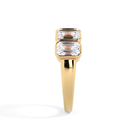A picture of a five stone diamond wedding ring with emerald cut diamonds that are bezel set in yellow gold on a white background with a side profile view.