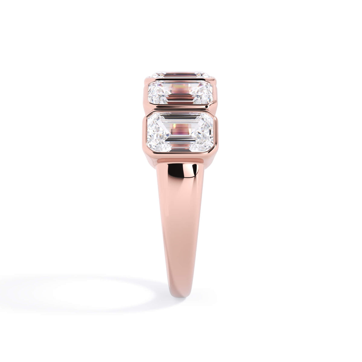 A picture of a five stone diamond wedding ring with emerald cut diamonds that are bezel set in rose gold on a white background with a side profile view.