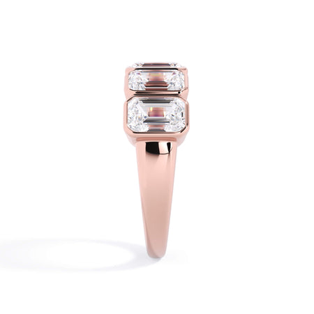 A picture of a five stone diamond wedding ring with emerald cut diamonds that are bezel set in rose gold on a white background with a side profile view.