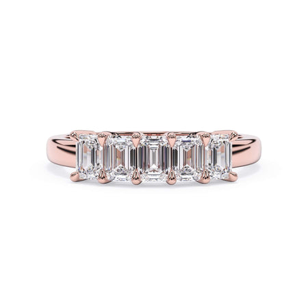 A picture of a five stone diamond wedding ring with emerald cut diamonds that are shared prong set in rose gold on a white background with the ring facing forward, lying down.