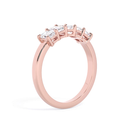 A picture of a five stone diamond wedding ring with emerald cut diamonds that are shared prong set in rose gold on a white background with a slightly angled, through the finger view.