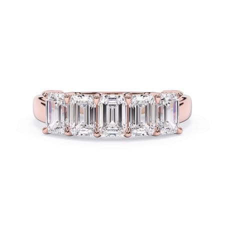 A picture of a five stone diamond wedding ring with emerald cut diamonds that are shared prong set in rose gold on a white background with the ring facing forward, lying down.