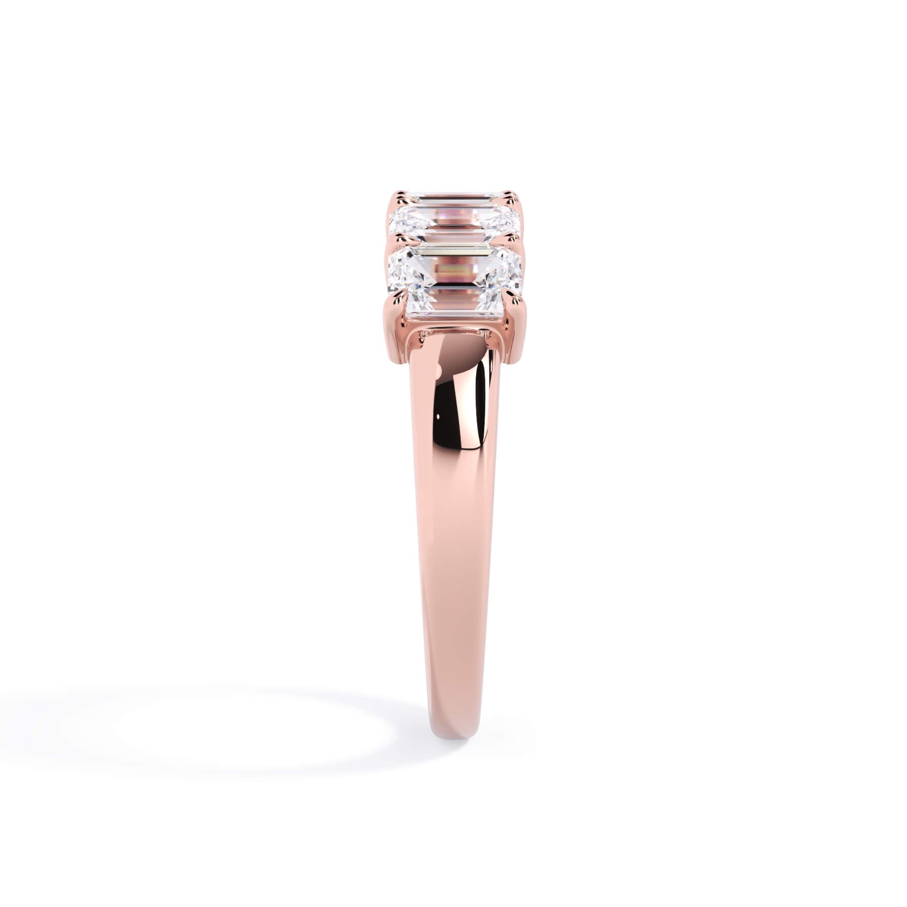 A picture of a five stone diamond wedding ring with emerald cut diamonds that are shared prong set in rose gold on a white background with a side profile view.
