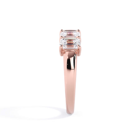A picture of a five stone diamond wedding ring with emerald cut diamonds that are shared prong set in rose gold on a white background with a side profile view.