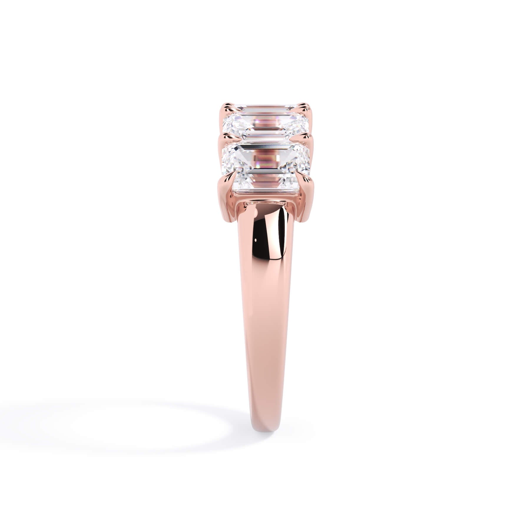 A picture of a five stone diamond wedding ring with emerald cut diamonds that are shared prong set in rose gold on a white background with a side profile view.