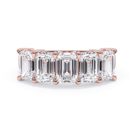 A picture of a five stone diamond wedding ring with emerald cut diamonds that are shared prong set in rose gold on a white background with the ring facing forward, lying down.