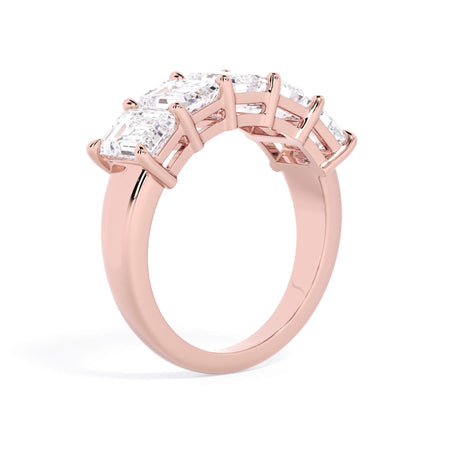 A picture of a five stone diamond wedding ring with emerald cut diamonds that are shared prong set in rose gold on a white background with a slightly angled, through the finger view.