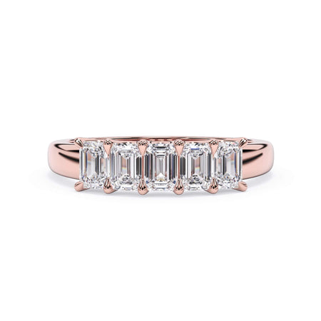 A picture of a five stone diamond wedding ring with emerald cut diamonds that are u prong set in rose gold on a white background with the ring facing forward, lying down.