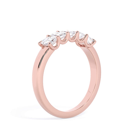 A picture of a five stone diamond wedding ring with emerald cut diamonds that are u prong set in rose gold on a white background with a slightly angled, through the finger view.