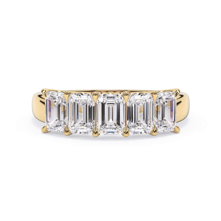 A picture of a five stone diamond wedding ring with emerald cut diamonds that are u prong set in yellow gold on a white background with the ring facing forward, lying down.