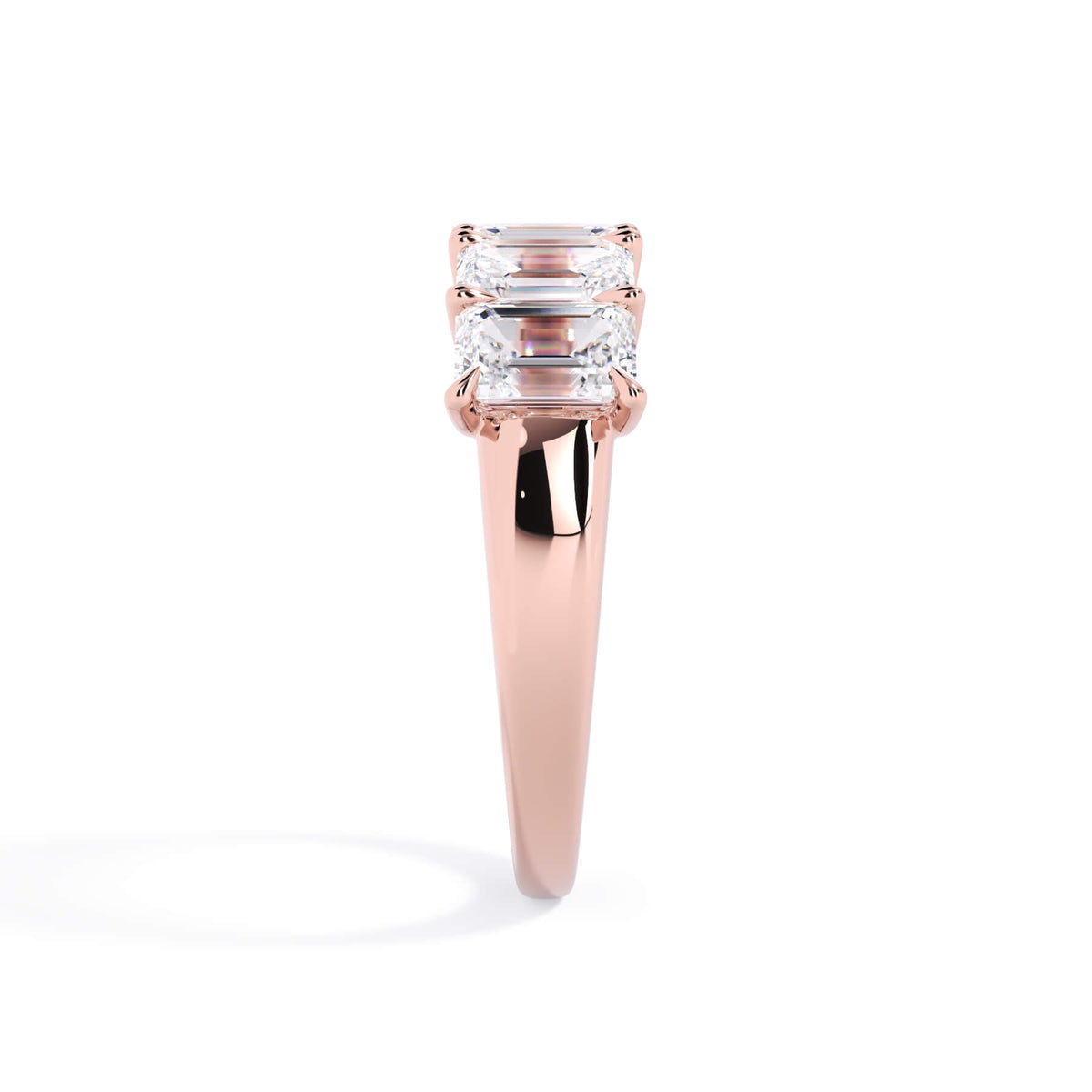 A picture of a five stone diamond wedding ring with emerald cut diamonds that are u prong set in rose gold on a white background with a side profile view.