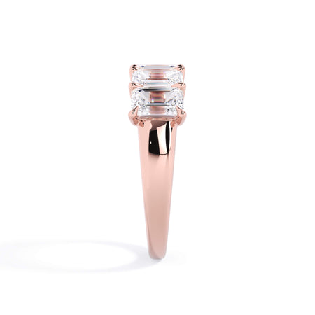 A picture of a five stone diamond wedding ring with emerald cut diamonds that are u prong set in rose gold on a white background with a side profile view.