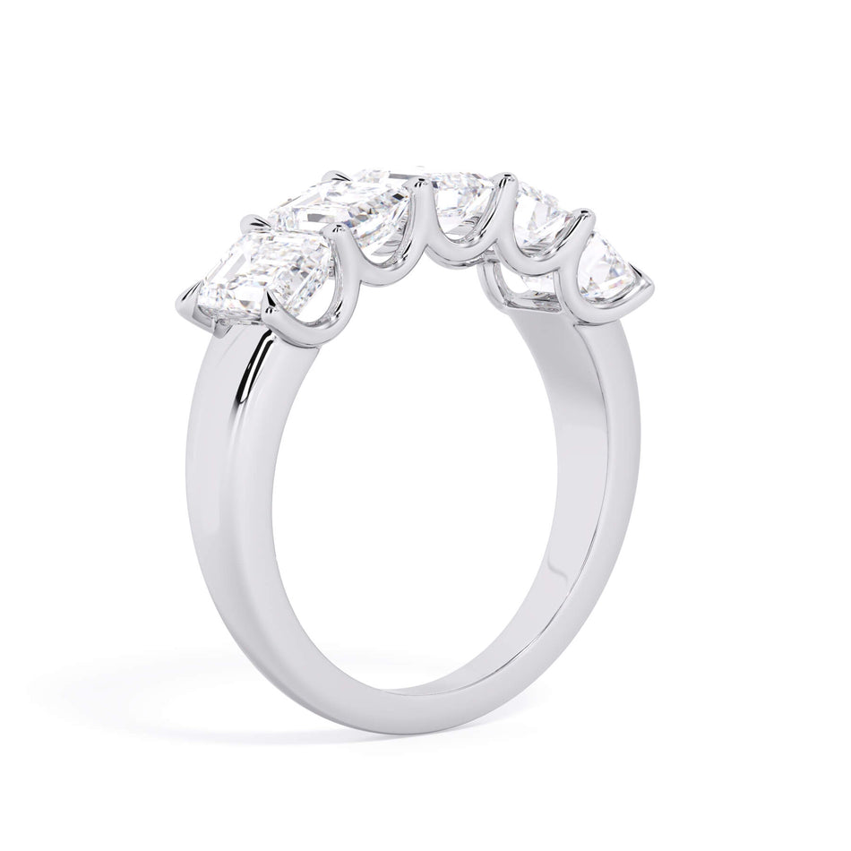 A picture of a five stone diamond wedding ring with emerald cut diamonds that are u prong set in white gold or platinum on a white background with a slightly angled, through the finger view.