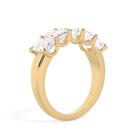 A picture of a five stone diamond wedding ring with emerald cut diamonds that are u prong set in yellow gold on a white background with a slightly angled, through the finger view.