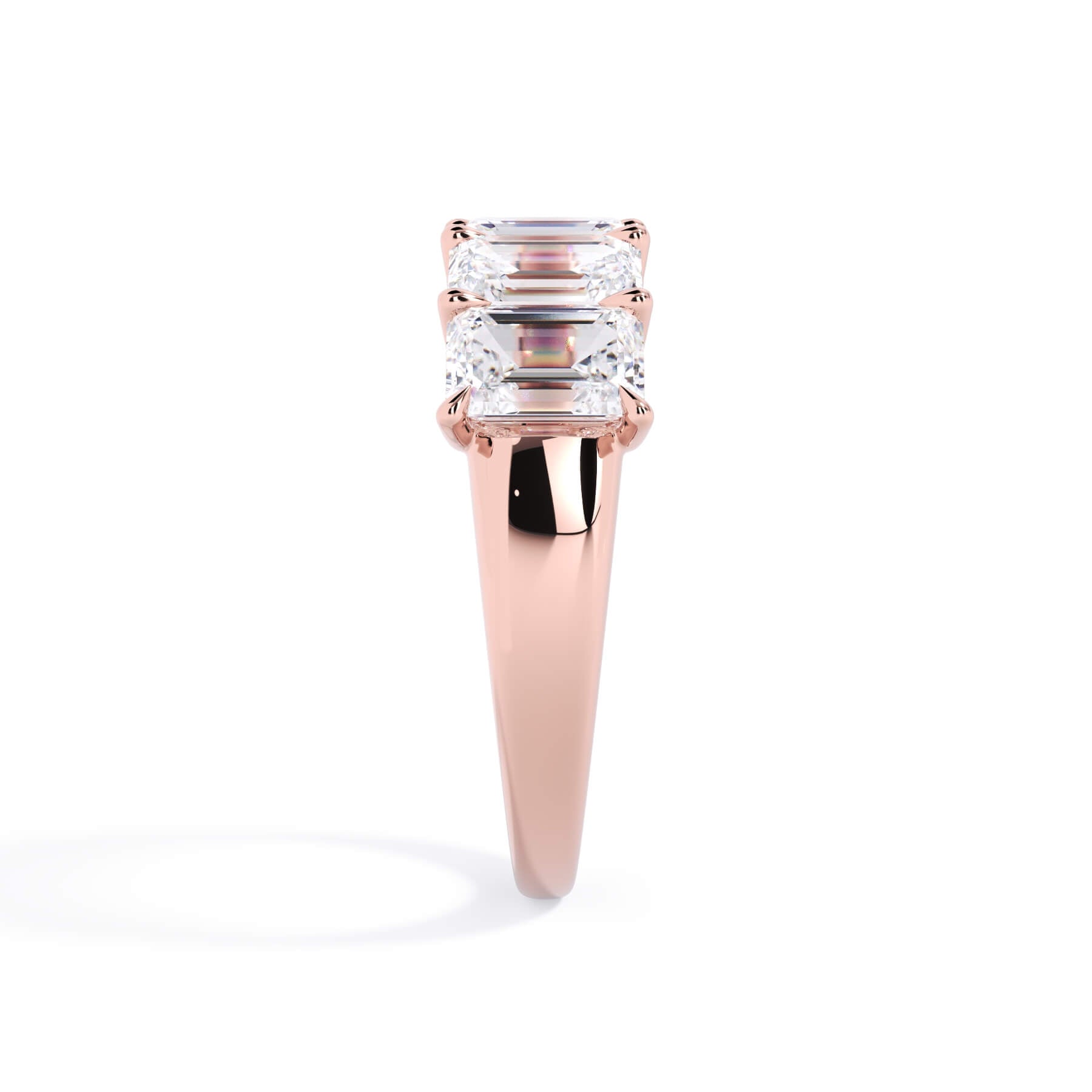 A picture of a five stone diamond wedding ring with emerald cut diamonds that are u prong set in rose gold on a white background with a side profile view.