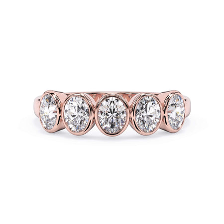 A picture of a five stone diamond wedding ring with oval shape diamonds that are bezel set in rose gold on a white background with the ring facing forward, lying down.