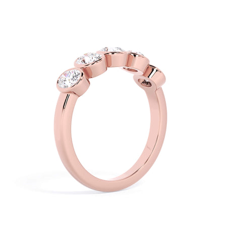 A picture of a five stone diamond wedding ring with oval shape diamonds that are bezel set in rose gold on a white background with a slightly angled, through the finger view.