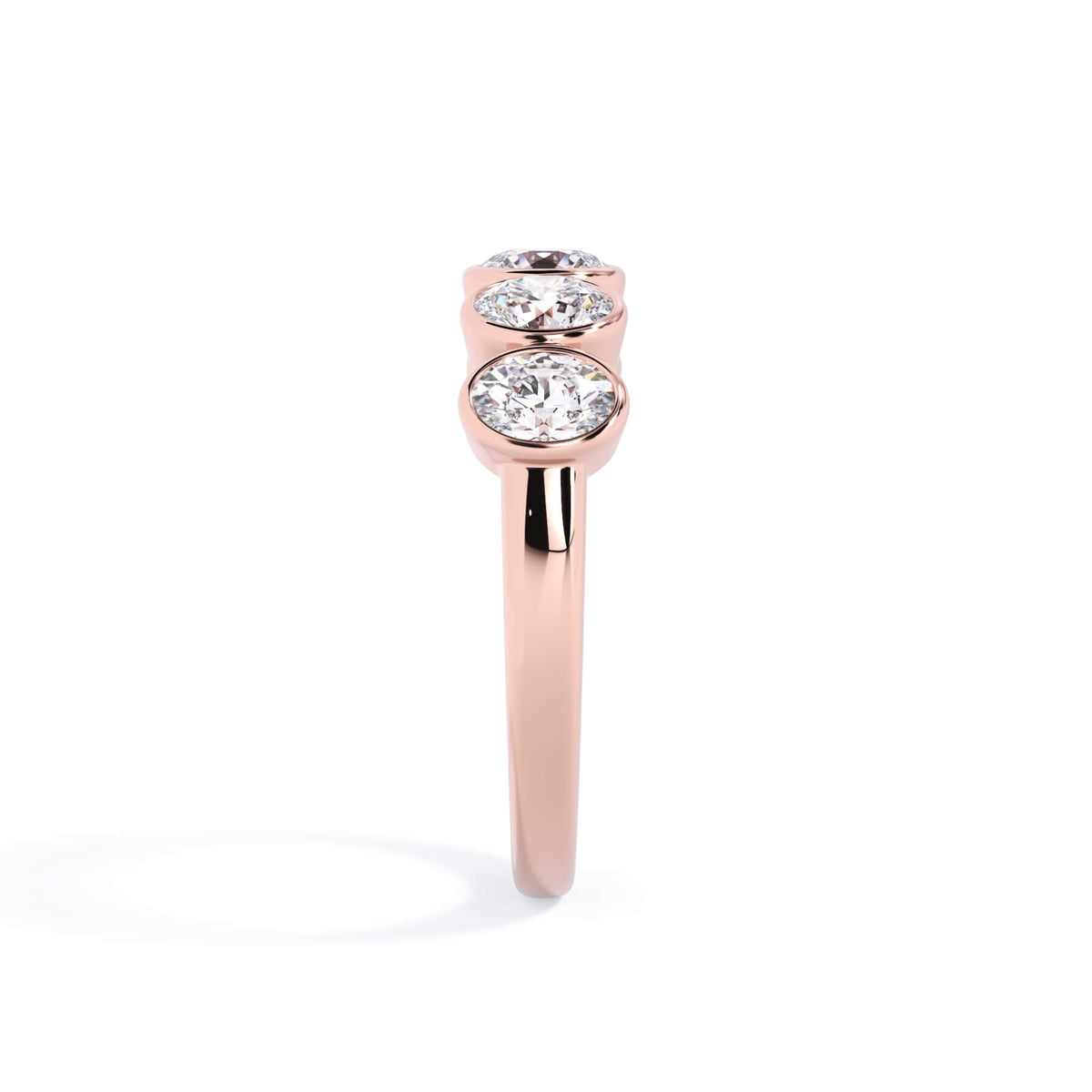 A picture of a five stone diamond wedding ring with oval shape diamonds that are bezel set in rose gold on a white background with a side profile view.