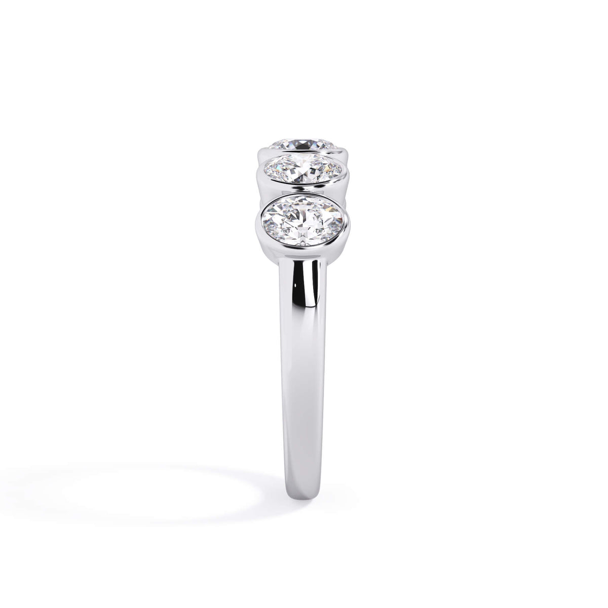 A picture of a five stone diamond wedding ring with oval shape diamonds that are bezel set in white gold or platinum on a white background with a side profile view.