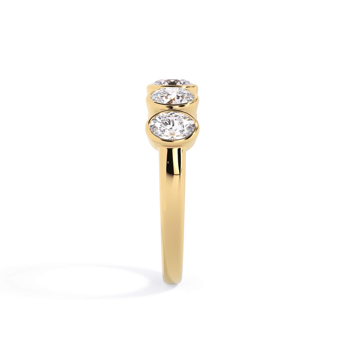 A picture of a five stone diamond wedding ring with oval shape diamonds that are bezel set in yellow gold on a white background with a side profile view.