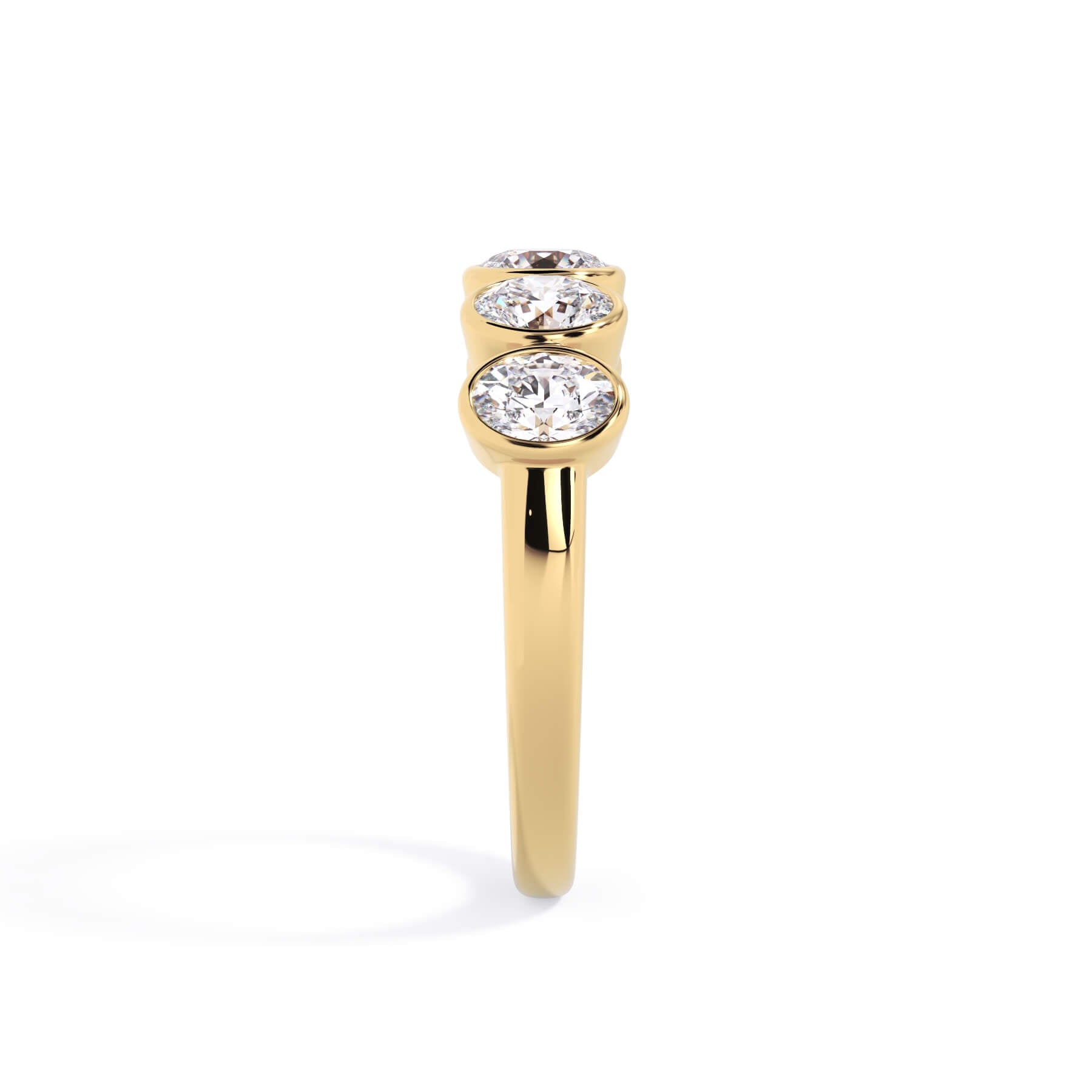 A picture of a five stone diamond wedding ring with oval shape diamonds that are bezel set in yellow gold on a white background with a side profile view.