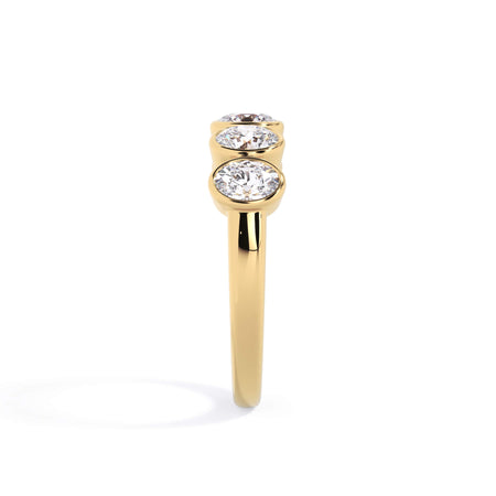 A picture of a five stone diamond wedding ring with oval shape diamonds that are bezel set in yellow gold on a white background with a side profile view.