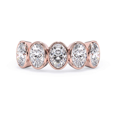 A picture of a five stone diamond wedding ring with oval shape diamonds that are bezel set in rose gold on a white background with the ring facing forward, lying down.