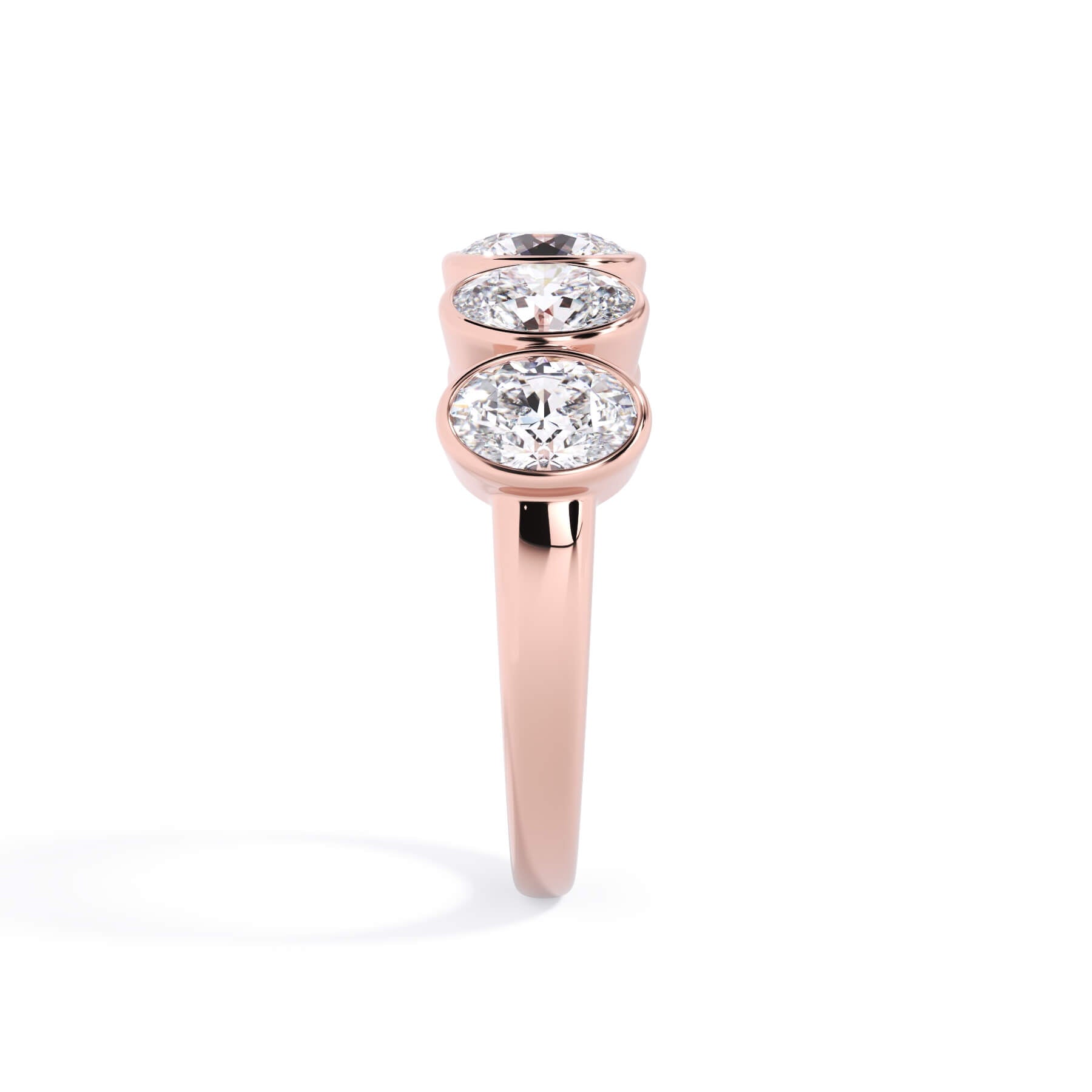 A picture of a five stone diamond wedding ring with oval shape diamonds that are bezel set in rose gold on a white background with a side profile view.