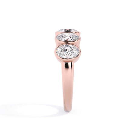 A picture of a five stone diamond wedding ring with oval shape diamonds that are bezel set in rose gold on a white background with a side profile view.