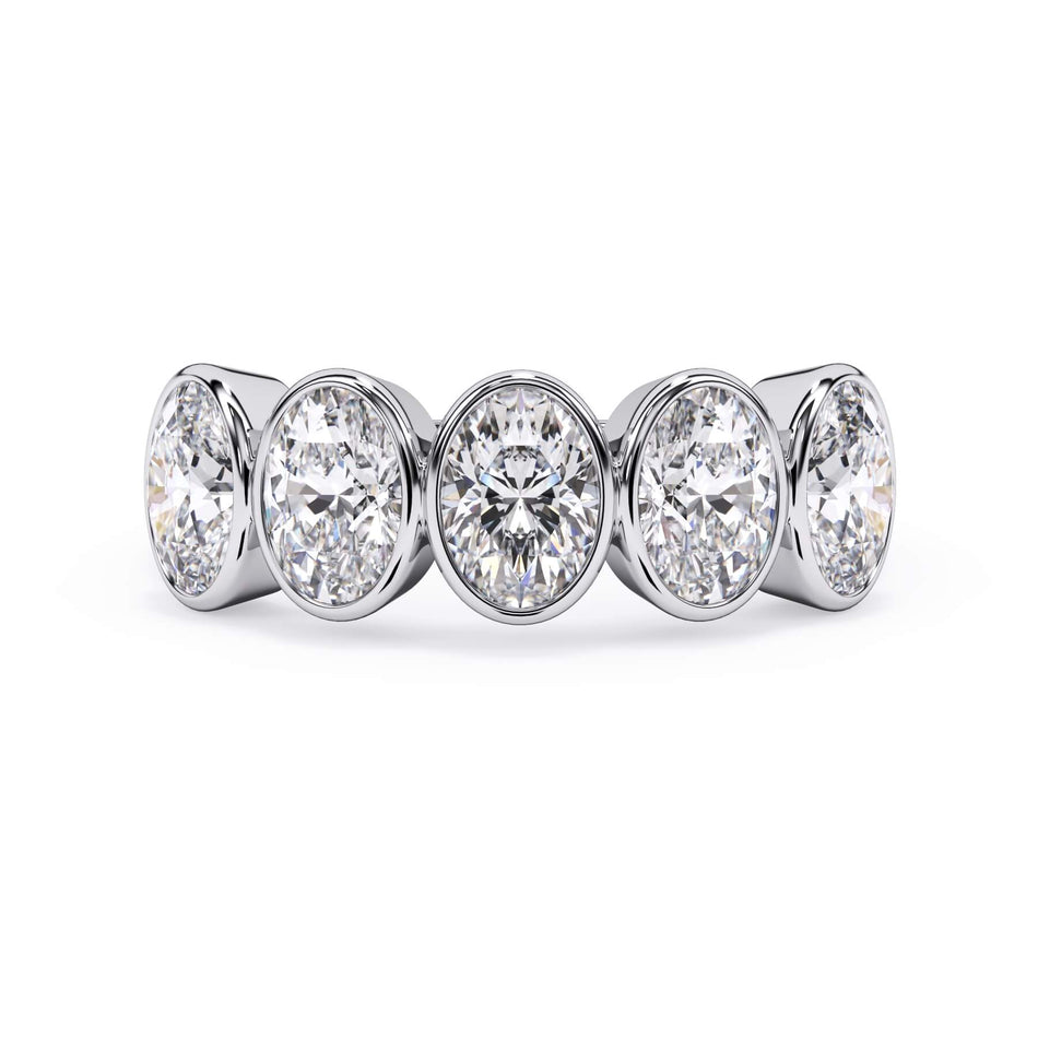 A picture of a five stone diamond wedding ring with oval shape diamonds that are bezel set in white gold or platinum on a white background with the ring facing forward, lying down.