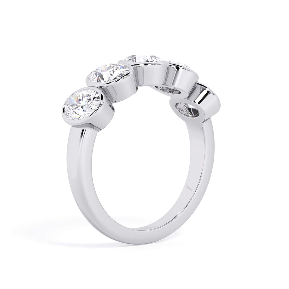 A picture of a five stone diamond wedding ring with oval shape diamonds that are bezel set in white gold or platinum on a white background with a slightly angled, through the finger view.