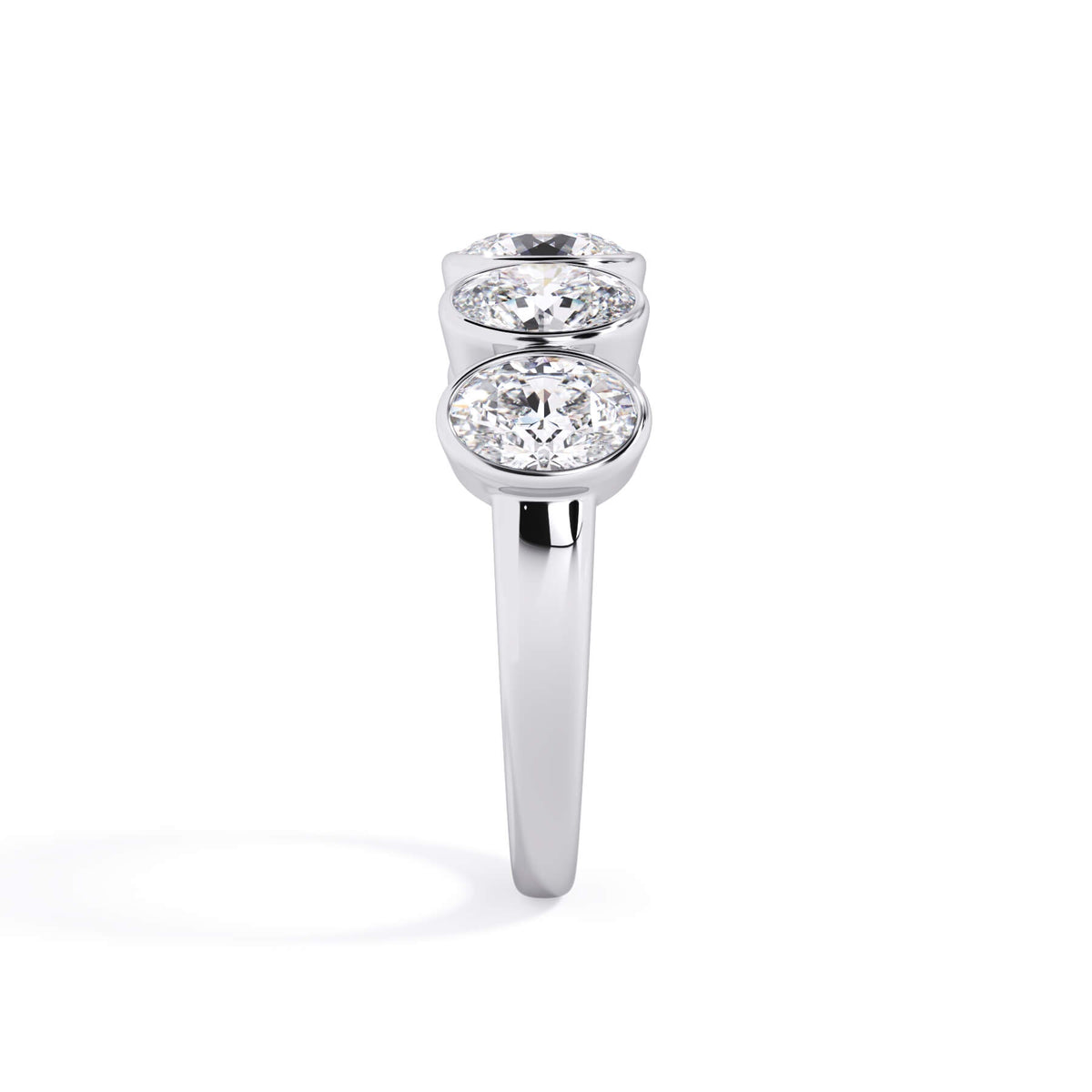 A picture of a five stone diamond wedding ring with oval shape diamonds that are bezel set in white gold or platinum on a white background with a side profile view.