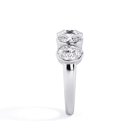 A picture of a five stone diamond wedding ring with oval shape diamonds that are bezel set in white gold or platinum on a white background with a side profile view.