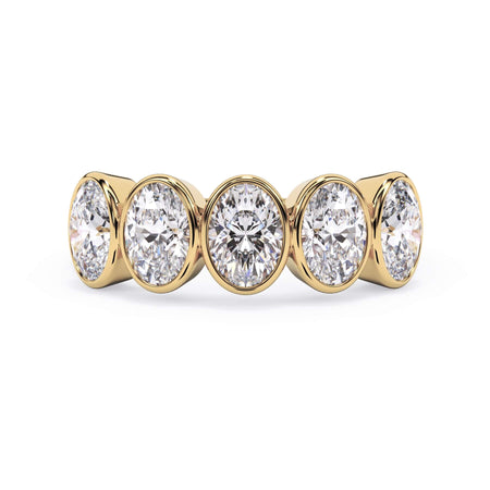 A picture of a five stone diamond wedding ring with oval shape diamonds that are bezel set in yellow gold on a white background with the ring facing forward, lying down.