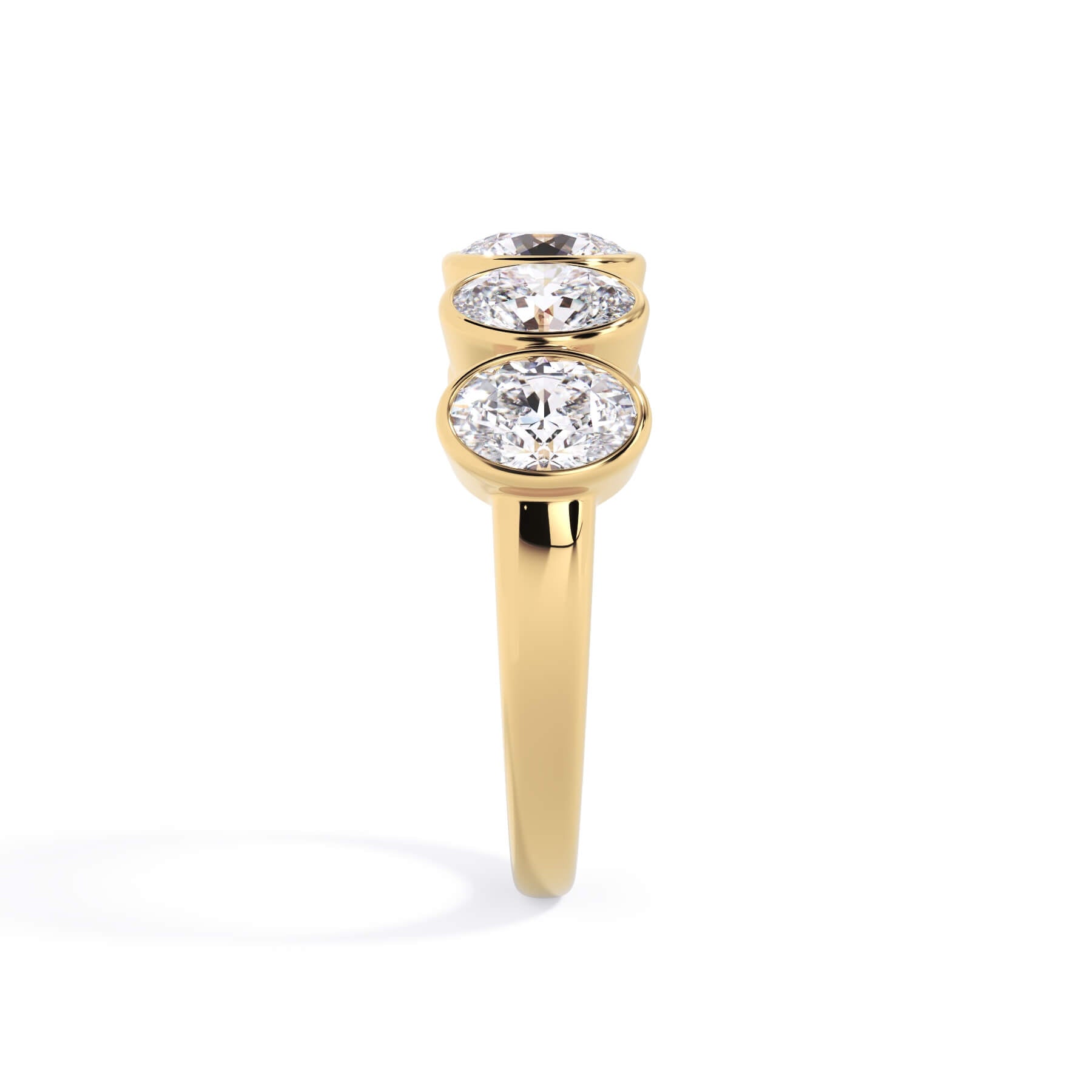 A picture of a five stone diamond wedding ring with oval shape diamonds that are bezel set in yellow gold on a white background with a side profile view.