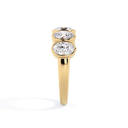A picture of a five stone diamond wedding ring with oval shape diamonds that are bezel set in yellow gold on a white background with a side profile view.