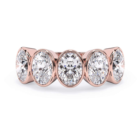 A picture of a five stone diamond wedding ring with oval shape diamonds that are bezel set in rose gold on a white background with the ring facing forward, lying down.
