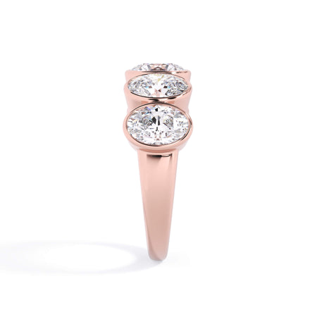 A picture of a five stone diamond wedding ring with oval shape diamonds that are bezel set in rose gold on a white background with a side profile view.