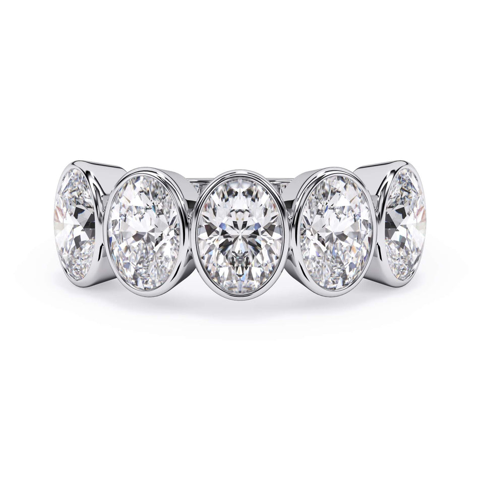 A picture of a five stone diamond wedding ring with oval shape diamonds that are bezel set in white gold or platinum on a white background with the ring facing forward, lying down.