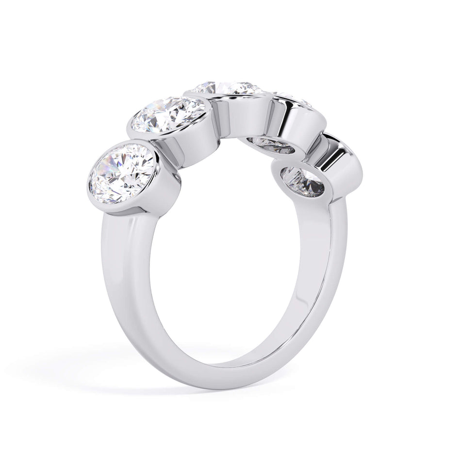 A picture of a five stone diamond wedding ring with oval shape diamonds that are bezel set in white gold or platinum on a white background with a slightly angled, through the finger view.