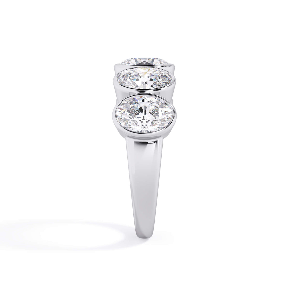 A picture of a five stone diamond wedding ring with oval shape diamonds that are bezel set in white gold or platinum on a white background with a side profile view.