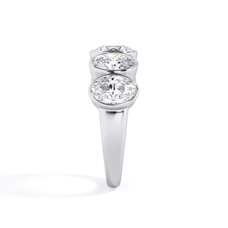 A picture of a five stone diamond wedding ring with oval shape diamonds that are bezel set in white gold or platinum on a white background with a side profile view.