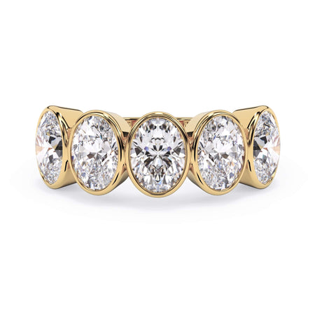 A picture of a five stone diamond wedding ring with oval shape diamonds that are bezel set in yellow gold on a white background with the ring facing forward, lying down.