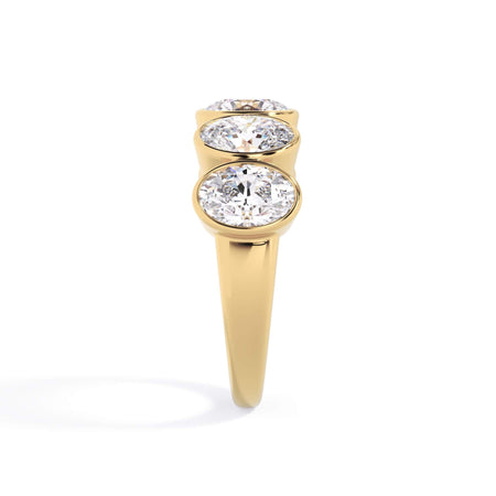A picture of a five stone diamond wedding ring with oval shape diamonds that are bezel set in yellow gold on a white background with a side profile view.