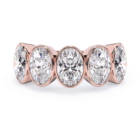 A picture of a five stone diamond wedding ring with oval shape diamonds that are bezel set in rose gold on a white background with the ring facing forward, lying down.